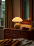 The Bloom Lamp glowing on a wooden dresser beside a mirror