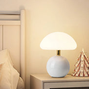 Bloom glass mushroom table lamp lit warm on a fluted nightstand beside a linen bed