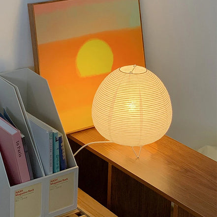 Haru rice paper lamp on a walnut shelf beside a sunset painting