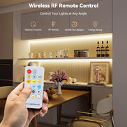 A hand holding the wireless remote in a kitchen lit by the COB strip under the cabinets