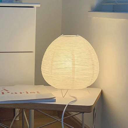 The Haru rice paper table lamp glowing warm on a white side table in a quiet corner