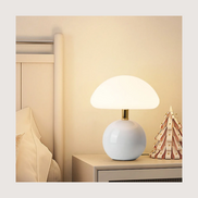 Bloom glass mushroom table lamp lit warm on a nightstand beside a linen bed