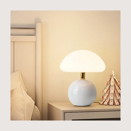 Bloom glass mushroom table lamp lit warm on a nightstand beside a linen bed